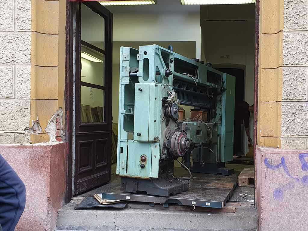 Nehézgép szállítás szűk ajtón keresztül padlóvédelemmel és görgőkkel